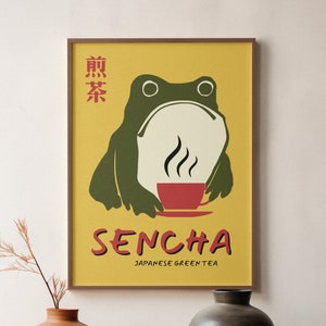 Puede incluir: Un póster enmarcado con fondo amarillo que presenta una rana verde sosteniendo una taza roja de té. El póster dice "Sencha Japanese Green Tea" y tiene caracteres japoneses en la esquina superior izquierda.