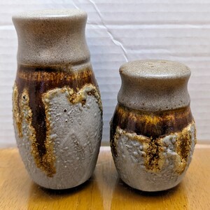 May include: Two ceramic salt and pepper shakers with a brown and gray glaze. The shakers have a textured surface and are hand-crafted.