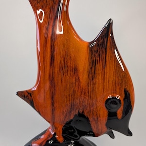 May include: A ceramic fish ornament with a glossy finish. The fish has a vibrant orange and black colour scheme with a textured pattern. The base is black and the fins are pointed. This decorative item is a unique home decor piece.