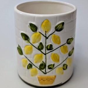 Puede incluir: Porta cubiertos de cerámica blanca con un diseño de limonero. El árbol tiene hojas verdes y limones amarillos. La maceta es amarilla con un borde verde.