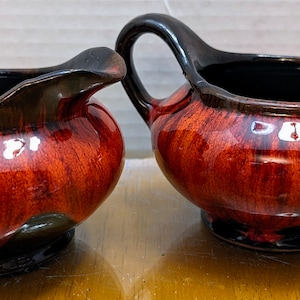 May include: A red and black ceramic creamer and sugar set with a swirled glaze pattern.