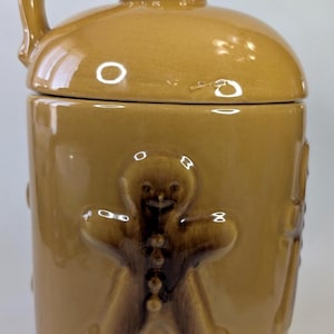 Può includere: Un barattolo per biscotti in ceramica marrone con manico e coperchio. Il barattolo presenta omini di pan di zenzero in rilievo e dettagli decorativi. Il barattolo è di colore marrone caldo e ha una finitura lucida. Il barattolo è progettato per conservare biscotti.