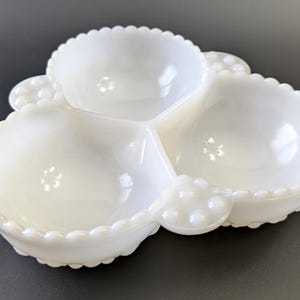 Peut inclure: Un plat de service blanc à trois compartiments. Chaque section est ronde avec un bord festonné et un petit groupe décoratif de points en relief. Le plat est en verre blanc opaque, idéal pour servir des collations ou des apéritifs.