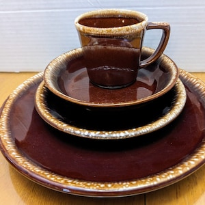 May include: A set of brown and white ceramic dishes with a brown and white ceramic mug. The dishes are nested together and the mug is sitting on top of the dishes.