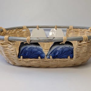 May include: Woven basket with a gray metal handle and ceramic accents. The basket features two blue and white ceramic inserts and two off-white tags. The handles have a blue and white striped pattern.