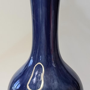 May include: A dark blue ceramic vase with a silver metallic glaze. The vase has a round body and a long, narrow neck.