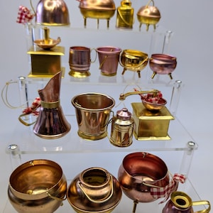 Può includere: Una collezione di ornamenti da cucina in miniatura in rame e ottone. Gli ornamenti sono disposti su tre livelli di un espositore in acrilico trasparente. Gli ornamenti includono pentole, padelle, brocche e altri utensili da cucina.