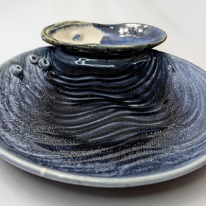 May include: A blue and white ceramic serving dish with a smaller dish on top. The larger dish has a wavy pattern and the smaller dish has a white interior.