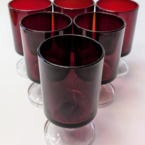 May include: Set of six stemmed shot glasses made of dark red glass with clear glass bases.