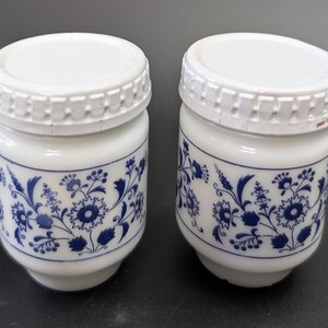 Può includere: Due barattoli in ceramica bianca con motivi floreali blu e coperchi in plastica bianca. I barattoli hanno una forma cilindrica con una base leggermente svasata. Il design floreale blu include fiori e foglie.