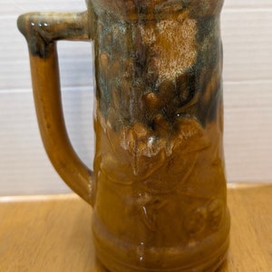 May include: A brown ceramic mug with a green glaze and a handle. The mug has a rustic, handmade look.
