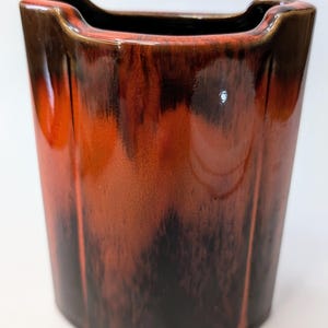 Peut inclure: Un vase en céramique de forme rectangulaire arrondie. Le vase est émaillé d'une couleur brune et orange avec un effet marbré.