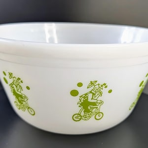 Puede incluir: Tazón blanco para mezclar con un diseño verde de personas montando bicicletas. El diseño incluye círculos y estrellas verdes.