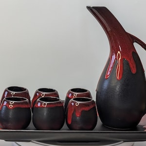 Può includere: Un vassoio da portata in ceramica nera con una glassa rossa, che comprende una caraffa in ceramica nera con una glassa rossa e sei piccole tazze in ceramica nera con una glassa rossa.