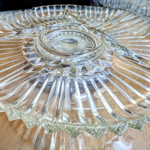 Puede incluir: Un plato de servir de vidrio transparente con cuatro secciones. El plato tiene una sección central elevada y un borde festoneado.