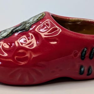 Peut inclure: Planteur en céramique rouge en forme de sabot avec un intérieur brun et un motif floral noir et bleu.