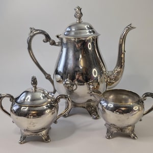 Peut inclure: Un service à thé argenté comprenant une théière, un sucrier avec couvercle et un pot à crème. La théière a un bec verseur incurvé et une anse ornée. Le sucrier et le pot à crème ont de petites anses et des pieds décoratifs.