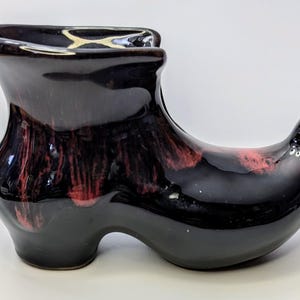 May include: A black ceramic boot planter with red and white glaze. The boot is shaped like a traditional Dutch clog.