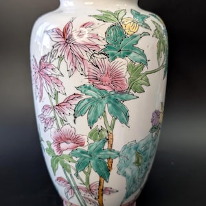 Peut inclure: Un vase en céramique blanc avec un motif floral. Le vase présente des fleurs et des feuilles roses, vertes et jaunes. La base du vase est rose. Le vase a une finition brillante et une forme arrondie.