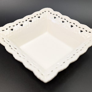 May include: A white ceramic square dish with a decorative lace-like border.