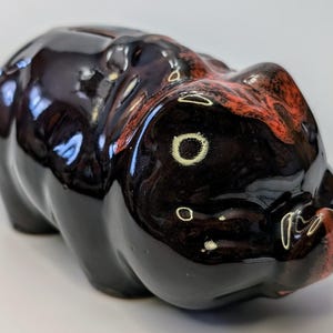 May include: A black ceramic piggy bank with red and white accents. The piggy bank is lying on its side with its snout facing the camera.