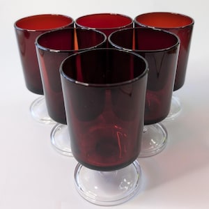 May include: A set of six ruby red stemmed glasses, arranged in a triangular pattern. Each glass has a cylindrical body and a clear, circular base. The interior of the glasses is a rich red, with a darker exterior. These glasses are suitable for serving drinks.