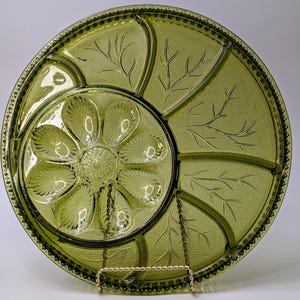 Könnte beinhalten: Eine grüne Glasservierplatte mit einem gewellten Rand und einem Perlenrand. Die Platte ist in sechs Abschnitte unterteilt, wobei ein zentraler Abschnitt sechs einzelne Vertiefungen aufweist. Die Platte hat ein Blattmotiv, das in das Glas geätzt ist.