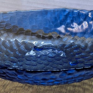 May include: A blue glass bowl with a textured, bumpy surface. The bowl is oval shaped and has a slight curve to the sides.