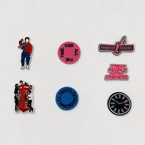 Könnte beinhalten: Eine Sammlung von sechs bestickten Aufnähern mit verschiedenen Motiven: eine Person in roter Jacke, eine rote Telefonzelle mit Figuren, ein runder rosa Aufnäher mit KISS ALL THE TIME, ein blauer mit DISCO OCCASIONALLY, ein schwarzer mit HANGOVER CHASING, ein rosa mit TREAT PEOPLE WITH KINDNESS und ein schwarzes Zifferblatt.