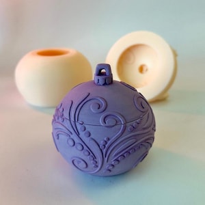 Può includere: Un ornamento natalizio viola con un design floreale a spirale. L'ornamento è realizzato in un materiale liscio e duro e ha un piccolo anello in cima per appenderlo.