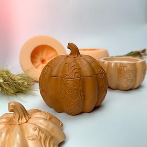 Op de afbeelding: Een verzameling pompoenvormige decoratieve items in verschillende tinten oranje en perzik. De centrale pompoen is een container met deksel en ingewikkelde reliëf bloemmotieven. Andere pompoenen zijn een kleine kom en een mal.