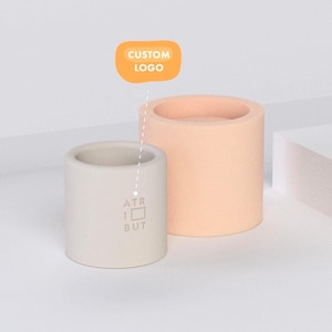 Può includere: Due contenitori cilindrici, uno grigio chiaro e l'altro color pesca, sono esposti su sfondo bianco. Il contenitore grigio ha il testo "ATR 1 BUT" stampato sopra. Un ovale giallo sopra i contenitori recita "CUSTOM LOGO".