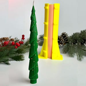 Puede incluir: Una vela verde con forma de árbol de Navidad con detalles dorados. Un molde amarillo y rosa en el fondo. La vela está decorada con pequeños puntos dorados. La vela es una decoración festiva.