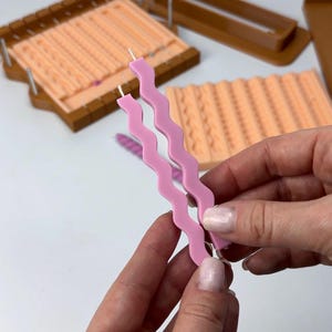 Puede incluir: Dos velas onduladas de color rosa claro con mechas blancas se sostienen. En el fondo, moldes de velas en tonos melocot&oacute;n y marr&oacute;n. Los moldes tienen patrones texturizados para hacer velas. Las velas miden unos 20 cm de largo.