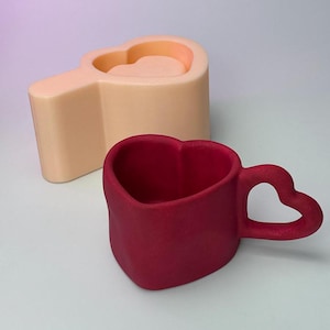 May include: A red heart-shaped mug with a heart-shaped handle. The mug is made of ceramic and has a smooth, glossy finish.