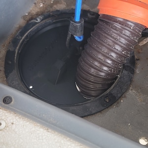 May include: A black round drain cover with the text "Quality Tested" visible. A black and orange hose is connected to the drain cover. A blue bungee cord is attached to the hose.