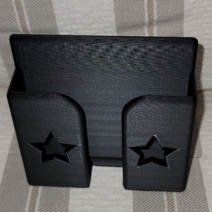 May include: Black plastic phone stand with two star cutouts. The stand is designed to hold a phone upright.