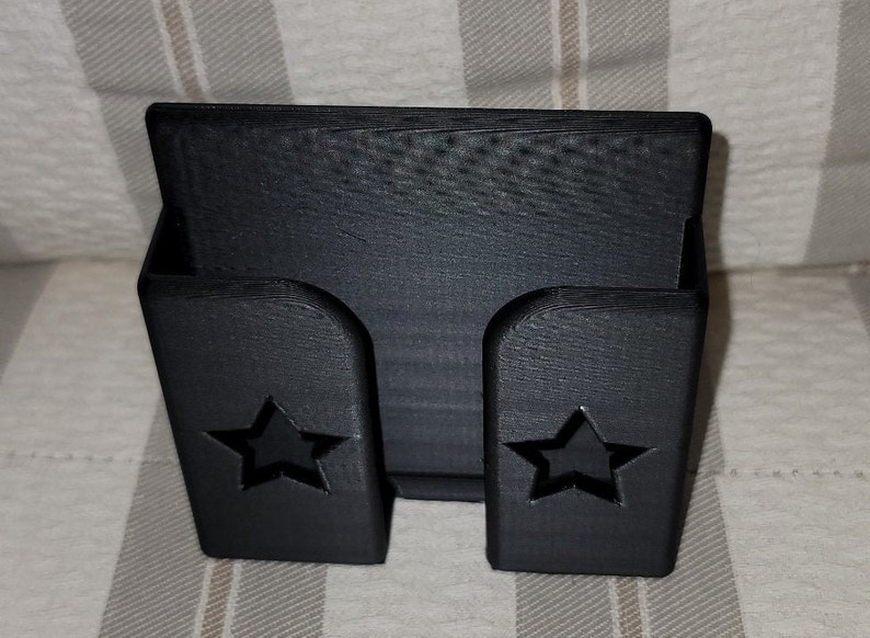 May include: Black plastic phone stand with two star cutouts. The stand is designed to hold a phone upright.