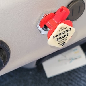 Könnte beinhalten: Ein roter und weißer Feststellbremshebel mit dem Text "PULL TO APPLY PARKING BRAKE PUSH TO RELEASE Bendix" darauf.