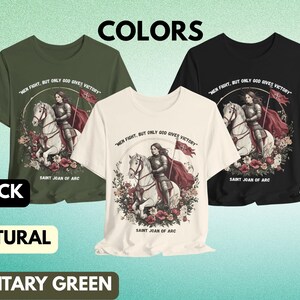 May include: Three t-shirts in black, natural, and military green with a graphic print of Saint Joan of Arc riding a white horse. The text "Men fight, but only God gives victory" is printed on each shirt.