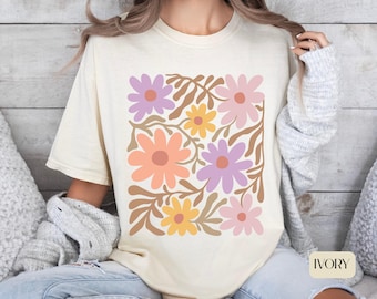 May include: Ivory-colored t-shirt featuring a square floral design. The design includes large flowers in shades of pink, orange, yellow, and purple, with brown leaf accents. The word "IVORY" is printed in a white rectangle at the bottom.