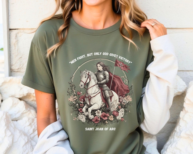 May include: Green t-shirt with a graphic of Saint Joan of Arc riding a white horse. The graphic includes the text "Men fight, but only God gives victory" and "Saint Joan of Arc".