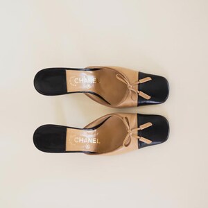 Op de afbeelding: Tweekleurige leren muiltjes in beige en zwart. De schoenen hebben een vierkante neus en een kleine strik. De merknaam "CHANEL" is op de binnenzool gedrukt. Stijlvolle instappers.