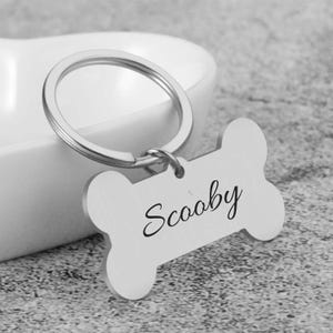 May include: Silver dog bone-shaped keychain with a silver key ring and the name "Scooby" engraved on the bone.