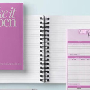 May include: Two pink spiral bound notebooks. The front cover of the first notebook says "make it happen" in white text. The front cover of the second notebook says "Monthly Budget Planner" in black text.