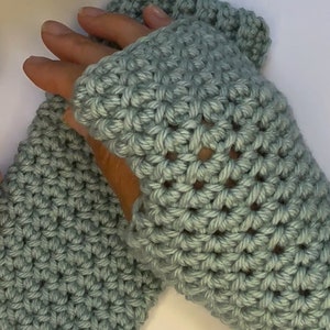 Puede incluir: Un par de guantes sin dedos de ganchillo de color azul claro. Los guantes tienen un patrón de punto sencillo y están hechos con un hilo suave.