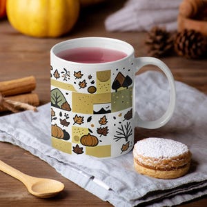 May include: A white ceramic mug featuring a repeating pattern of autumn-themed illustrations including orange pumpkins, brown fallen leaves, green trees, and mountain silhouettes arranged in a grid of yellow and white rectangular blocks.