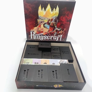 Könnte beinhalten: Ein Brettspiel-Box-Set mit dem Titel "Kingscraft" auf der Vorderseite. Die Box zeigt eine Fantasy-Illustration eines Kriegers und einer feurigen Landschaft. Im Inneren sind schwarze Spielsteine und Karten ordentlich angeordnet.