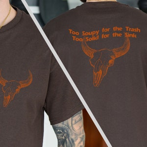 May include: Brown t-shirt with a brown bull skull graphic and the text "Too Soupy for the Trash Too Solid for the Sink".