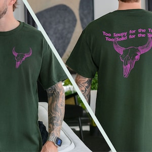 May include: A dark green t-shirt with a pink bull skull graphic on the front and the text "Too Soupy for the Trash Too Solid for the Sink" on the back.